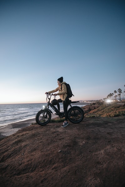 在棕色夹克的男人骑在黑色的摩托车在棕色沙附近的水域
